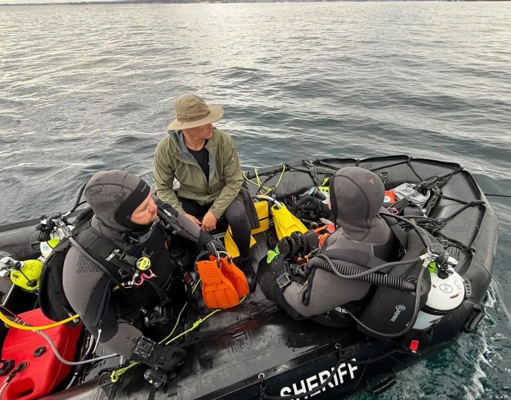 Rescue team members in a sheriff's boat preparing to recover a body from the ocean.
