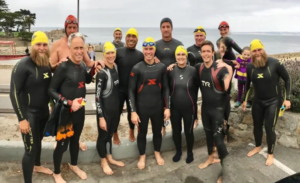 Erica Fox and other members of the Kelp Krawlers swim group pose in wetsuits by the ocean.