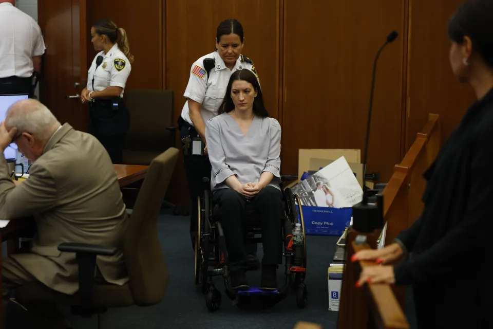 Lindsay Clancy in a wheelchair, being pushed by a police officer, during her murder trial.