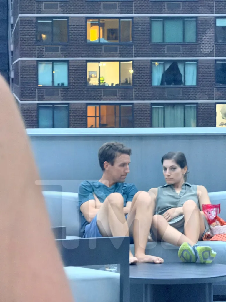 Patrick Clancy and Rachel Danis sitting on a couch on a rooftop with a building in the background.