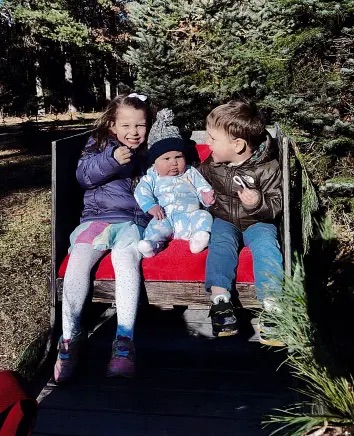 Three young children sitting together on a red bench outdoors.