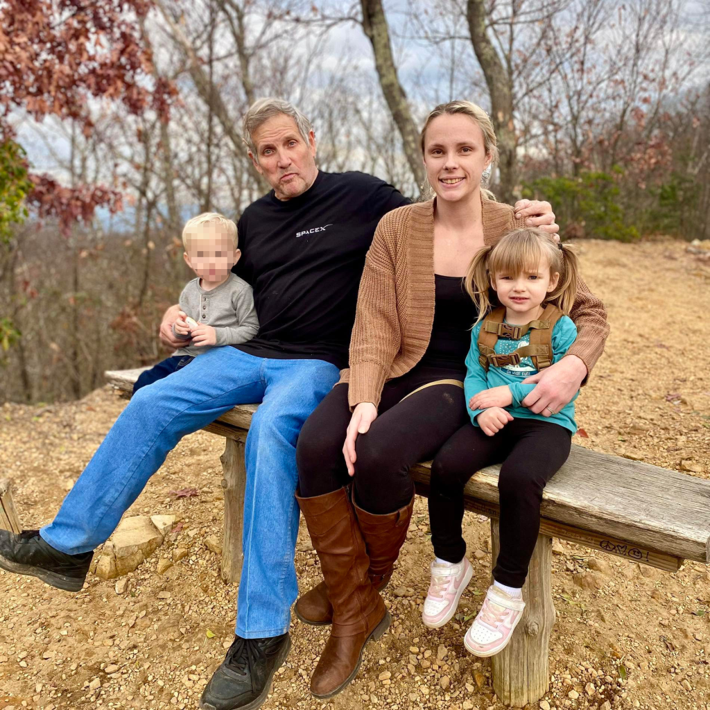 A man, a woman, and two children sitting on a wooden bench outdoors.