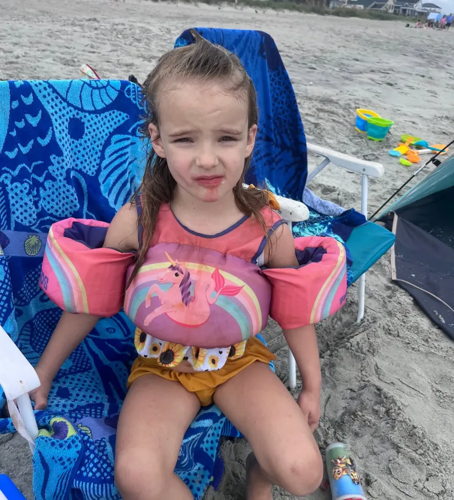 Saylor Hayes, a nonverbal 5-year-old girl, sitting in a beach chair, wearing a unicorn-patterned swim flotation device over a bathing suit.