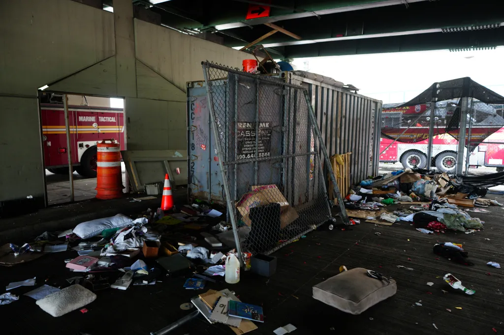 Various items are strewn inside and outside an open cargo container at a homeless encampment under the West Side Highway.